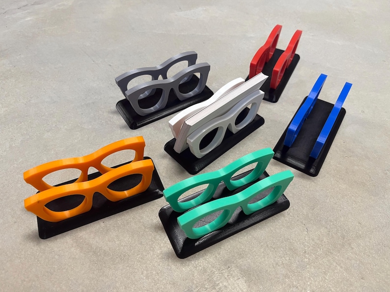 Glasses Business Card Holders sitting on concrete.  Colors are grey, blue, teal, red, white and orange.