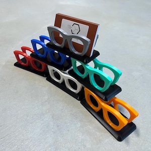 Glasses Business Card Holder stacked in a triangle sitting on concrete.  Colors are grey, blue, teal, red, white and orange.