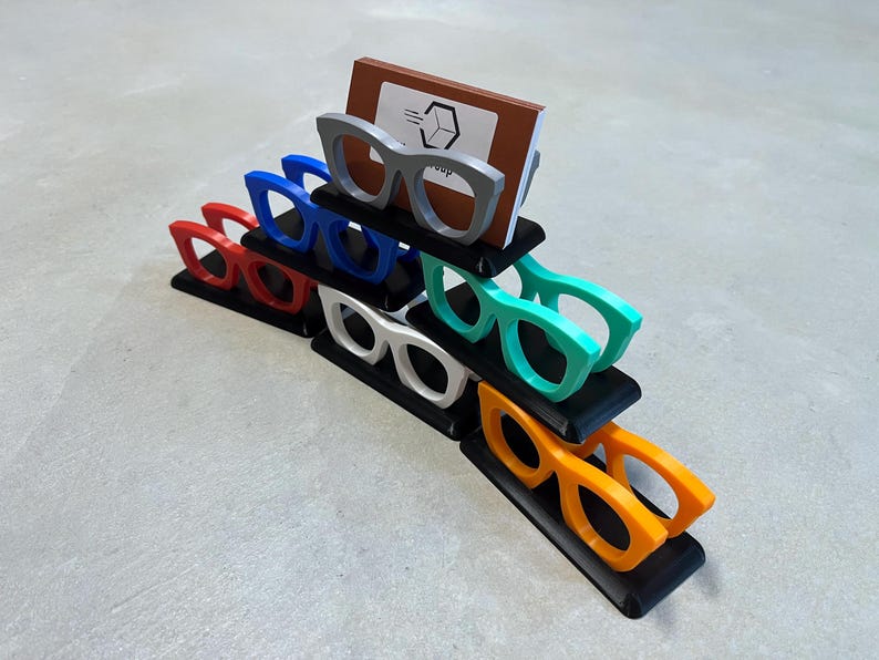 Glasses Business Card Holder stacked in a triangle sitting on concrete.  Colors are grey, blue, teal, red, white and orange.