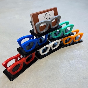 Glasses Business Card Holders sitting on concrete.  Colors are grey, blue, teal, red, white and orange.