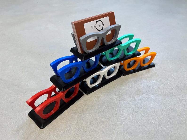 Glasses Business Card Holders sitting on concrete.  Colors are grey, blue, teal, red, white and orange.