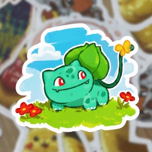 Puede incluir: Una pegatina con un personaje de dibujos animados verde con ojos rojos, un bulbo en la espalda y una flor en la cola. El personaje está sobre hierba verde con flores rojas, un cielo azul y nubes blancas. Otras pegatinas están en el fondo.