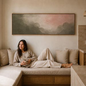 May include: A long, rectangular landscape painting in a wooden frame, featuring a soft, atmospheric depiction of rolling hills or clouds in muted shades of sage green, gray, and a pale, dusty pink glow across the upper right portion of the canvas.