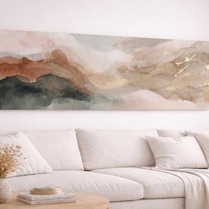 Può includere: Una lunga tela rettangolare raffigurante un paesaggio astratto. L'opera d'arte presenta una tavolozza di toni tenui, tra cui sfumature di marrone, verde e oro, creando un'estetica serena e naturale. La tela è montata sopra un divano bianco.