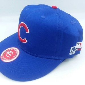 May include: A blue baseball cap with a red "C" logo and a red button on top. The cap has a flat brim and a white and red MLB logo on the side. The cap has a sticker that says "OC Sports Youth".