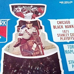 Puede incluir: Un objeto de colección azul con temática de hockey con el logotipo de los New York Rangers, un portero en acción y texto que indica los playoffs de la Copa Stanley de 1971 con los Chicago Black Hawks y los Toronto Maple Leafs. La esquina superior derecha dice "ONE DOLLAR".
