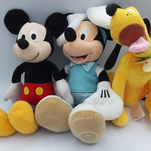 Peut inclure: Trois peluches de personnages Disney : Mickey Mouse en noir, rouge et jaune ; un deuxième Mickey Mouse en bleu et blanc ; et Pluto, un chien jaune avec une langue rose et un collier vert. Les jouets sont doux et câlins.