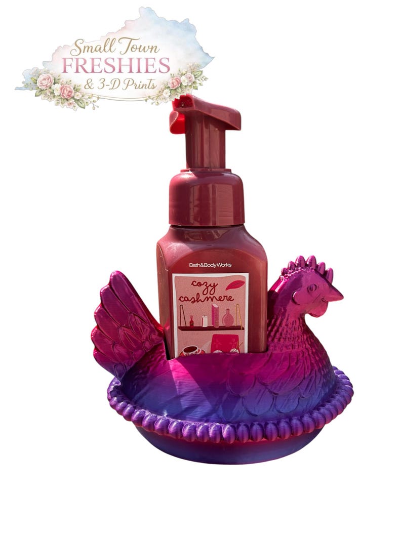 May include: A burgundy soap dispenser with a red pump sits in a 3D-printed hen-shaped holder. The holder is a gradient of purple and pink. The soap bottle has a label that reads "cozy cashmere". The image also includes the text "Small Town Freshies & 3-D Prints".
