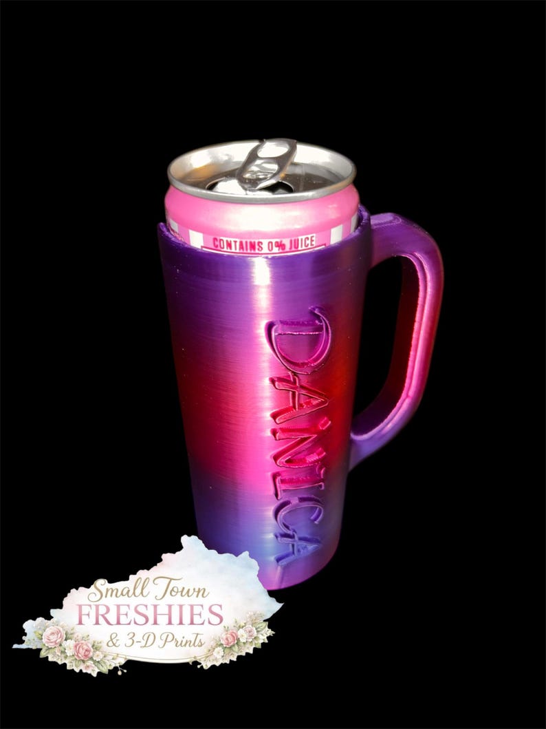 May include: A gradient purple and pink mug with the name "Danica" embossed on the side, holding a pink beverage can. The can reads "Contains 0% Juice." The mug has a handle and is set against a black background.