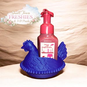 May include: A blue chicken-shaped soap holder with a pink soap dispenser. The soap dispenser has a pink pump and a label that reads "cozy cashmere." The image also includes text that says "Small Town Freshies & 3-D Prints."