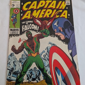 Puede incluir: Portada de cómic vintage de Capitán América. La ilustración muestra al Capitán América con su escudo y al Halcón con un traje verde y naranja. El cómic se titula "Capitán América" y "¡La llegada del Halcón!"