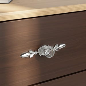 May include: Close-up of a drawer with a decorative crystal knob. The knob is silver-toned with a clear, faceted crystal center and leaf-shaped accents. The drawer is dark brown wood.