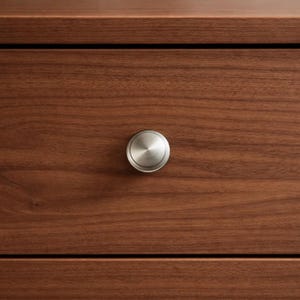 May include: Close-up of a wooden drawer with a brushed nickel knob. The drawer is made of dark brown wood with visible grain. The knob is circular and centered on the drawer front.