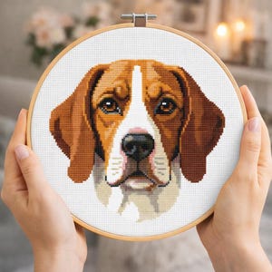 May include: A cross-stitch embroidery hoop depicting a beagle dog's portrait. The dog has brown and white fur, with a focused expression. The embroidery is set in a wooden hoop, showcasing a handmade craft.