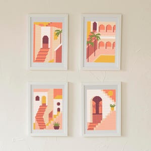 Puede incluir: Cuatro impresiones artísticas enmarcadas con un diseño geométrico. Cada impresión presenta una fachada de edificio con escaleras, arcos y palmeras en tonos melocotón, coral y amarillo. Las impresiones se exhiben en una pared texturizada de color blanco roto.