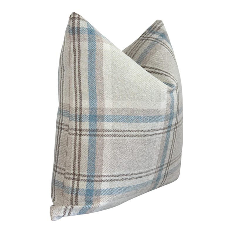Peut inclure: Un coussin carr&eacute; avec un motif &agrave; carreaux dans des tons bleu clair, beige et blanc. Le tissu pr&eacute;sente un aspect textur&eacute; avec des lignes horizontales et verticales qui se croisent pour former un motif &agrave; grille classique sur toute la surface.