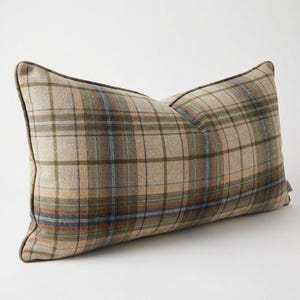 May include: A rectangular throw pillow featuring a plaid pattern in shades of beige, olive green, and muted blue. The pillow has a structured shape with piped edges along the seams, showcasing a woven texture throughout the fabric surface.