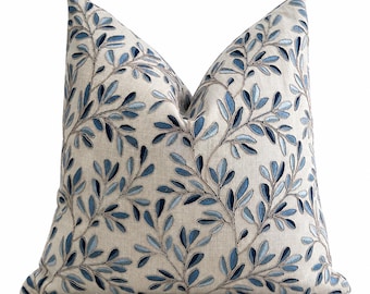 Peut inclure: Un coussin carré avec un tissu de base beige clair rappelant le lin, orné d'un motif brodé de branches et de feuilles traînantes dans diverses nuances de bleu, allant du bleu ciel clair au bleu marine profond, sur toute la surface avant.