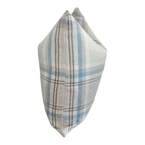 Peut inclure: Un coussin carr&eacute; avec un motif &agrave; carreaux compos&eacute; de lignes entrecrois&eacute;es dans des tons bleu clair, beige et blanc. Le tissu pr&eacute;sente un aspect textur&eacute; et le coussin est pr&eacute;sent&eacute; sous un angle lat&eacute;ral, soulignant sa forme structur&eacute;e.