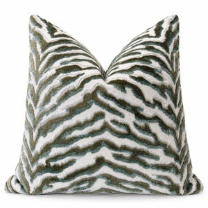 May include: A square throw pillow featuring a textured, raised zebra stripe pattern in shades of deep forest green, sage, and off-white. The fabric has a plush, velvet-like appearance with a distinct pile that creates depth across the surface.