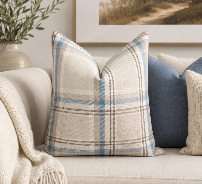 Peut inclure: Un coussin carr&eacute; avec un motif &agrave; carreaux tiss&eacute; dans des tons bleu clair, beige et blanc. Le tissu pr&eacute;sente un tissage textur&eacute; visible, et le motif se compose de lignes horizontales et verticales qui s'entrecroisent pour former une grille.