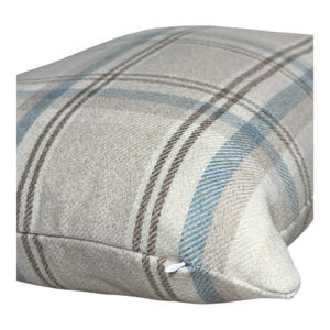 Peut inclure: Un coussin rectangulaire pr&eacute;sentant un motif &agrave; carreaux tiss&eacute; dans des tons beige, bleu clair et marron. Le tissu a un aspect textur&eacute; semblable &agrave; de la laine avec une fermeture &eacute;clair blanche visible situ&eacute;e le long du bord inf&eacute;rieur de la housse.