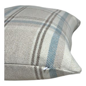 Peut inclure: Un coussin carr&eacute; avec un motif &agrave; carreaux tiss&eacute; dans des tons beige, bleu clair et marron fonc&eacute;. Le tissu pr&eacute;sente une texture serg&eacute;e diagonale visible. Une petite tirette de fermeture &eacute;clair blanche est visible sur le bord inf&eacute;rieur.