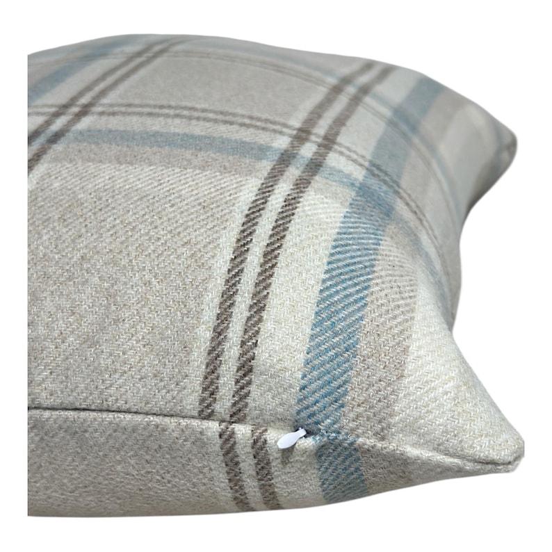 Peut inclure: Un coussin carr&eacute; avec un motif &agrave; carreaux tiss&eacute; dans des tons beige, bleu clair et marron fonc&eacute;. Le tissu pr&eacute;sente une texture serg&eacute;e diagonale visible. Une petite tirette de fermeture &eacute;clair blanche est visible sur le bord inf&eacute;rieur.