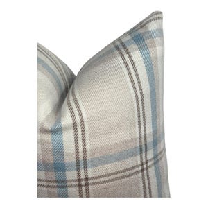 Peut inclure: Un coussin carr&eacute; avec un motif &agrave; carreaux tiss&eacute; dans des tons doux de bleu clair, beige et marron. Le tissu pr&eacute;sente une texture serg&eacute;e diagonale visible sur tout le motif, cr&eacute;ant une apparence structur&eacute;e avec des lignes nettes et crois&eacute;es.