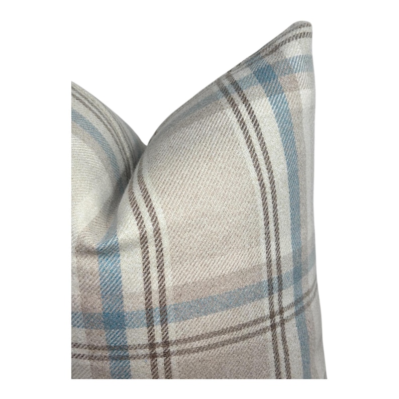 Peut inclure: Un coussin carr&eacute; avec un motif &agrave; carreaux tiss&eacute; dans des tons doux de bleu clair, beige et marron. Le tissu pr&eacute;sente une texture serg&eacute;e diagonale visible sur tout le motif, cr&eacute;ant une apparence structur&eacute;e avec des lignes nettes et crois&eacute;es.