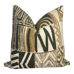May include: Square cushion with a patchwork design. The cushion features geometric patterns in black, olive green, tan, and cream. The patterns include stripes, zigzags, and abstract shapes, creating a textured appearance. Measurements are in centimeters.