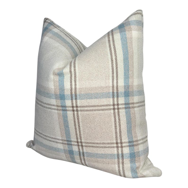 Peut inclure: Un coussin carr&eacute; avec un motif &agrave; carreaux dans des tons doux de bleu clair, beige et blanc. Le tissu pr&eacute;sente une texture tiss&eacute;e visible avec des lignes horizontales et verticales qui se croisent pour former un motif &agrave; grille classique.