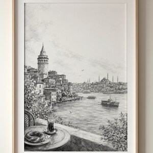 May include: A black and white pencil sketch print in a light wood frame depicting a coastal city view with the Galata Tower, a waterfront, boats, and a foreground table featuring a glass of tea and a circular pastry on a plate.