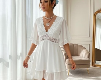 May include: A white dress with a V-neckline, lace detailing, and short, flared sleeves. The dress has a tiered skirt and is accessorized with jewelry. The dress is a summer or spring style.