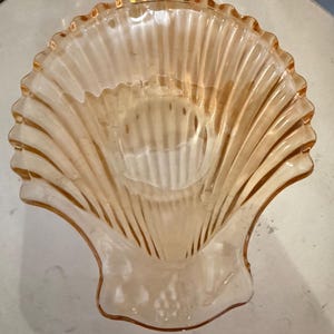 May include: A translucent, light amber-coloured glass bowl shaped like a large scallop shell. The bowl features a ribbed, fan-like texture radiating from the base to the scalloped, wavy rim, creating a decorative, shell-inspired vessel design.