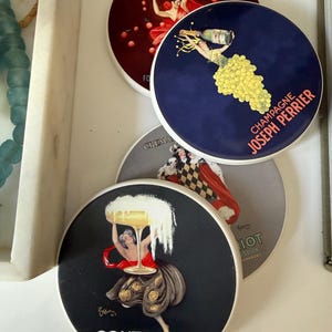 May include: Set of four round coasters with vintage-style illustrations. One coaster features a woman with a champagne bottle, another with a dancer, and two others with similar designs. Text includes "CONTRATTO" and "JOSEPH PERRIER".