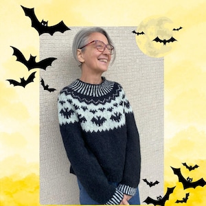 Puede incluir: Un suéter azul oscuro con un diseño de murciélagos en azul claro y blanco. El suéter tiene cuello y puños acanalados. El fondo tiene un degradado amarillo con siluetas de murciélagos y una luna llena, creando un tema de Halloween.