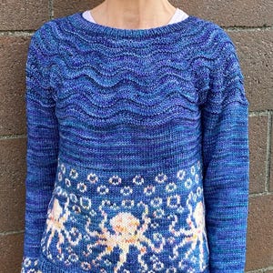 May include: A blue knit sweater with a wave pattern across the upper chest and octopus design on the lower portion. The octopus design is in shades of peach and white. The sweater has long sleeves and a round neckline.