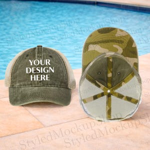 Puede incluir: Dos gorras de béisbol. Una es verde oliva con la parte trasera de malla y el texto "YOUR DESIGN HERE". La otra es de camuflaje. Ambas gorras se muestran sobre un fondo de agua azul.