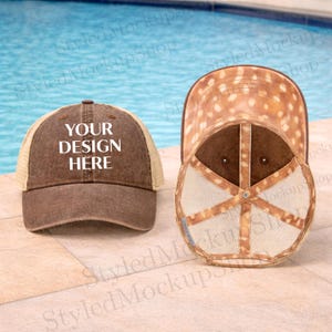 Puede incluir: Dos gorras de camionero marrones. Una gorra tiene un panel frontal marrón con el texto "YOUR DESIGN HERE" en blanco. La otra gorra está volteada, revelando un patrón de ciervo en la parte inferior de la visera y un interior marrón.
