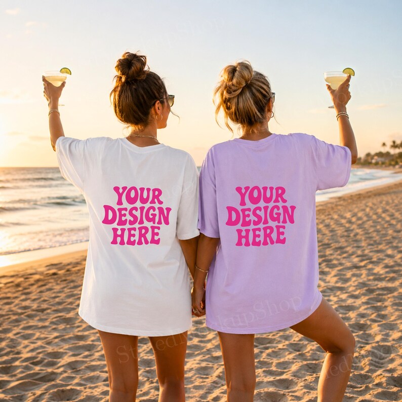 Puede incluir: Dos camisetas holgadas, una blanca y otra lavanda, con el texto "YOUR DESIGN HERE" en rosa. Las camisetas se usan en una playa al atardecer. Cada persona sostiene un c&oacute;ctel.