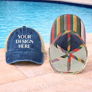 Puede incluir: Dos gorras de béisbol. Una es azul marino con una parte trasera de malla y el texto "YOUR DESIGN HERE" en blanco. La otra gorra tiene un patrón de rayas colorido. Las gorras se muestran sobre una superficie de piedra con una piscina en el fondo.