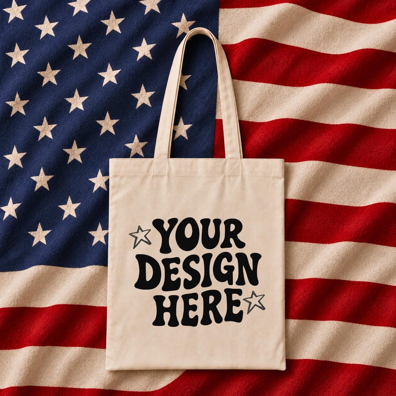 Puede incluir: Una bolsa de mano color crema con el texto "YOUR DESIGN HERE" en negro, sobre un fondo de la bandera estadounidense. La bolsa tiene dos asas y un dise&ntilde;o sencillo.