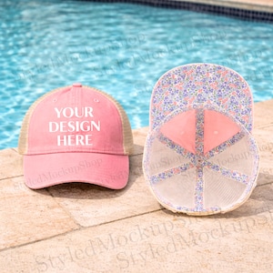 Puede incluir: Gorra de camionero rosa con el texto "YOUR DESIGN HERE". La gorra tiene una parte trasera de malla y una parte inferior con estampado floral. La gorra está sobre una superficie de piedra junto a una piscina.