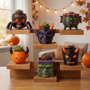 Peut inclure: Un présentoir en bois à plusieurs niveaux contenant six jardinières décoratives. Les pots présentent divers motifs, dont un crâne noir avec des pattes d'araignée, un diable à cornes violettes, un chaudron vert, une créature orange à cornes, un monstre vert et un démon noir.
