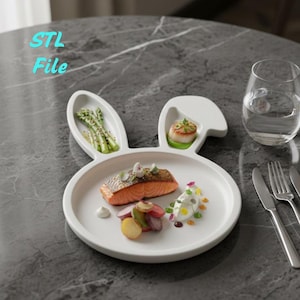 Può includere: Un piatto in ceramica bianca a forma di coniglio con un pasto gourmet. Il piatto contiene salmone, verdure e una capasanta. Un bicchiere d'acqua e posate sono sul tavolo. Il testo "STL File" è nell'immagine.