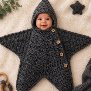 Peut inclure: Une gigoteuse pour bébé en forme d'étoile, crochetée en gris anthracite foncé avec une capuche pointue. Le vêtement présente une ouverture frontale diagonale fixée par quatre boutons en bois clair. La texture est uniforme sur tout l'ensemble.