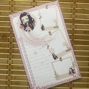 May include: A pink and white notepad with anime-style illustrations and floral details. The notepad has a to-do list section with checkboxes and a section for notes. The design includes images of a character with black hair and pink accents.