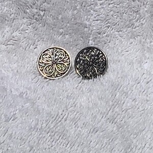May include: Two decorative buttons with intricate floral designs. One button is gold-toned, and the other is dark gray. The buttons are round and feature a detailed, openwork pattern, suitable for sewing or crafts.
