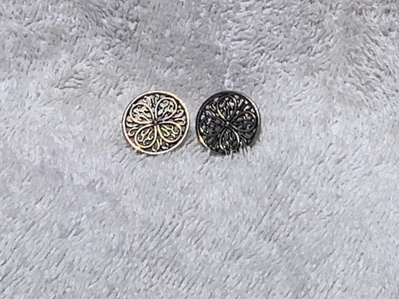 May include: Two decorative buttons with intricate floral designs. One button is gold-toned, and the other is dark gray. The buttons are round and feature a detailed, openwork pattern, suitable for sewing or crafts.